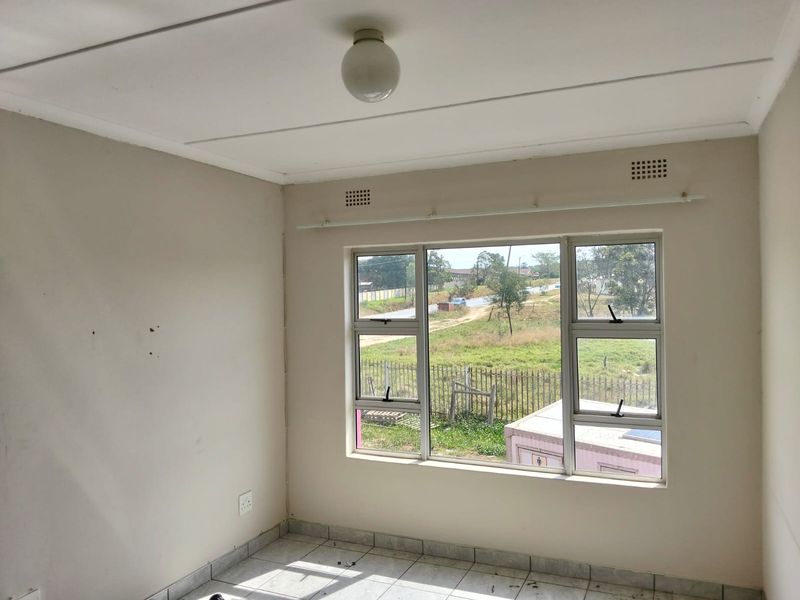 An empty bedroom featuring tiled flooring, neutral walls, and aluminium-framed windows with a view of the surrounding area.