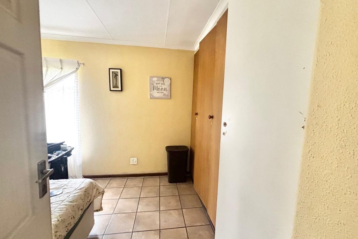 A bedroom featuring tiled flooring and built-in wooden cupboards, offering functional storage space and natural light.