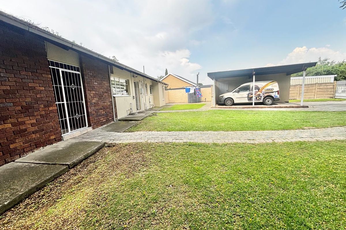Rear view of the property featuring a brick facade, paved walkway, established lawn, and a covered carport structure.