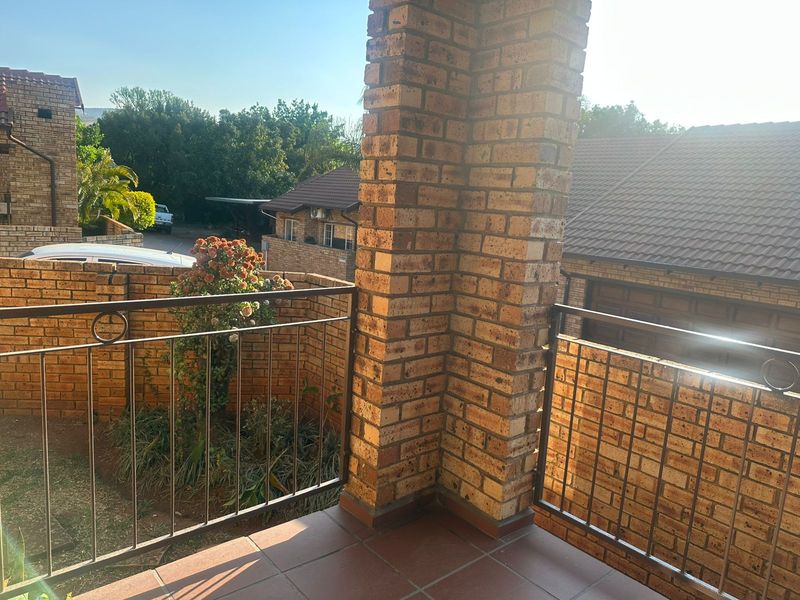 A covered balcony featuring brick pillar construction, tiled flooring, and metal balustrades, overlooking the surrounding townhouse complex.