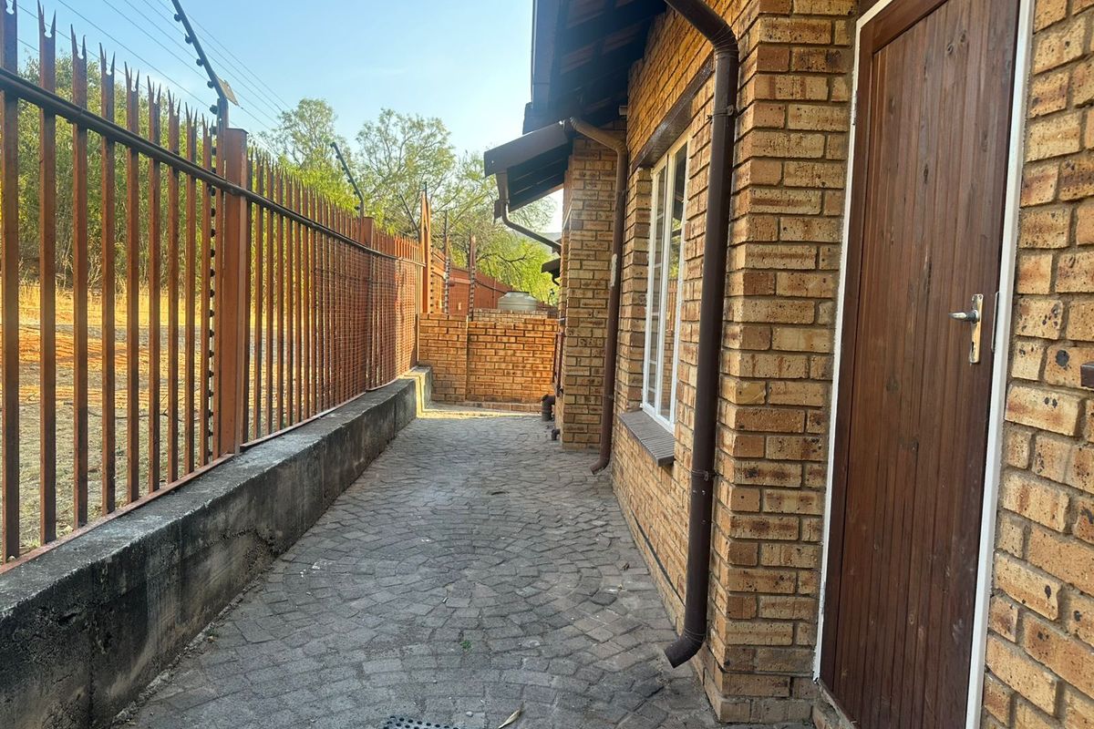 A side exterior walkway featuring face brick walls, paved flooring, and secure metal fencing with integrated electric security wires.