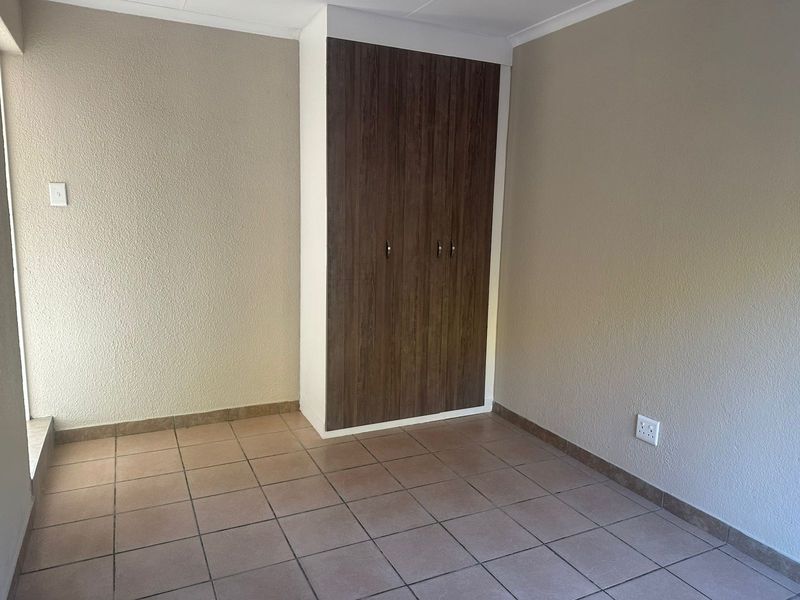 A clean, empty bedroom featuring neutral walls, tiled flooring, and a built-in wooden wardrobe.