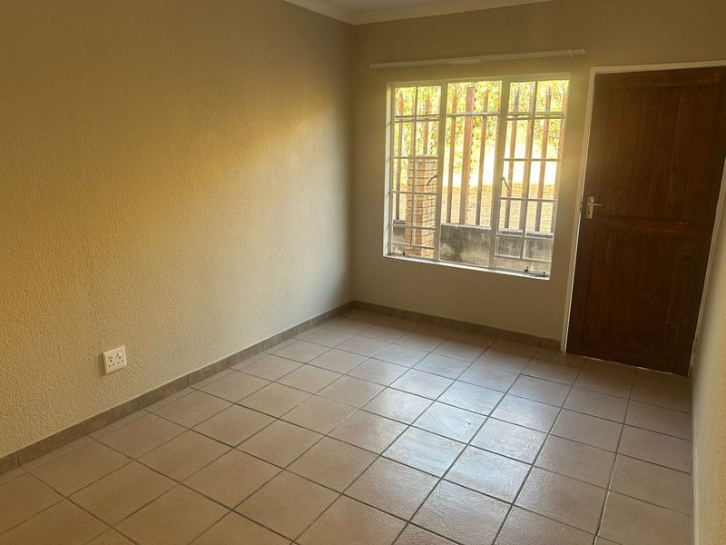 A vacant bedroom featuring neutral wall finishes, tiled flooring, a timber door, and a window fitted with security bars.