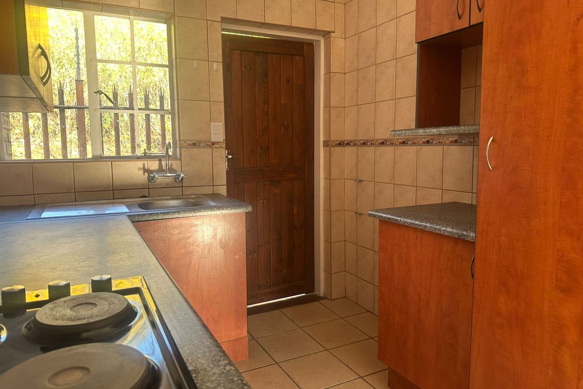 A functional kitchen featuring built-in timber cabinetry, laminate countertops, an electric hob, and tiled finishes throughout, providing a practical workspace.
