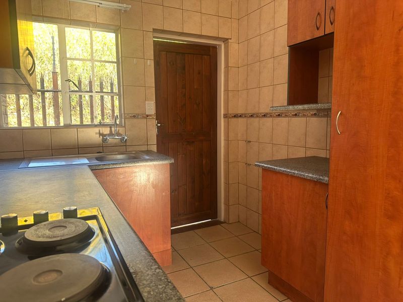 A functional kitchen featuring built-in timber cabinetry, laminate countertops, an electric hob, and tiled finishes throughout, providing a practical workspace.
