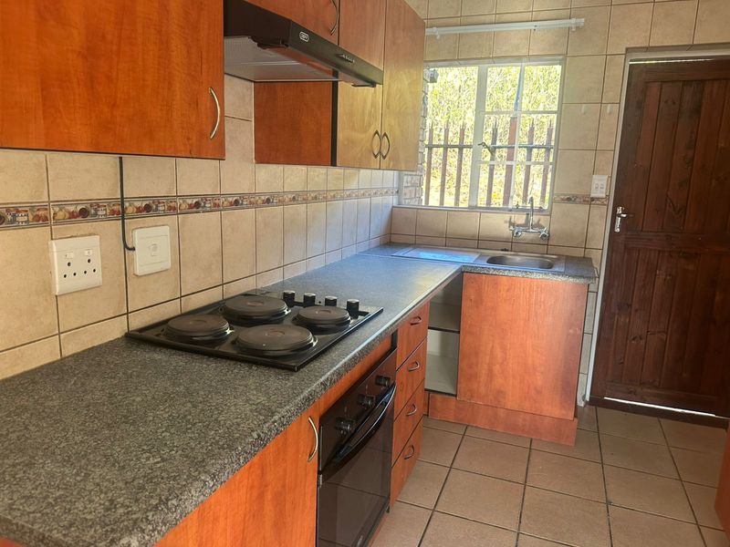 Functional kitchen featuring laminate cabinetry, built-in electric hob and oven, tiled splashbacks, and a stainless steel sink with direct exterior access.