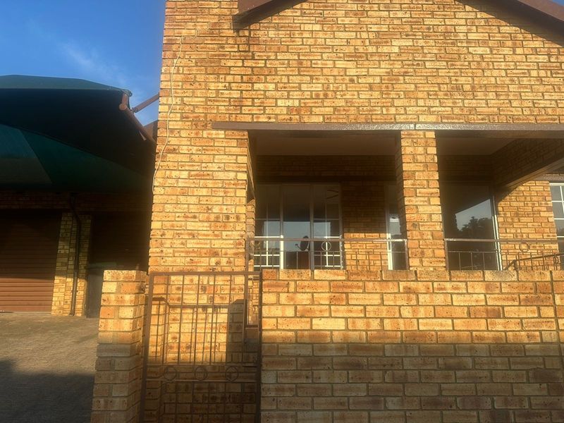 Front elevation of a face brick townhouse featuring a covered patio area, metal security fixtures, and an adjacent shade cloth carport.