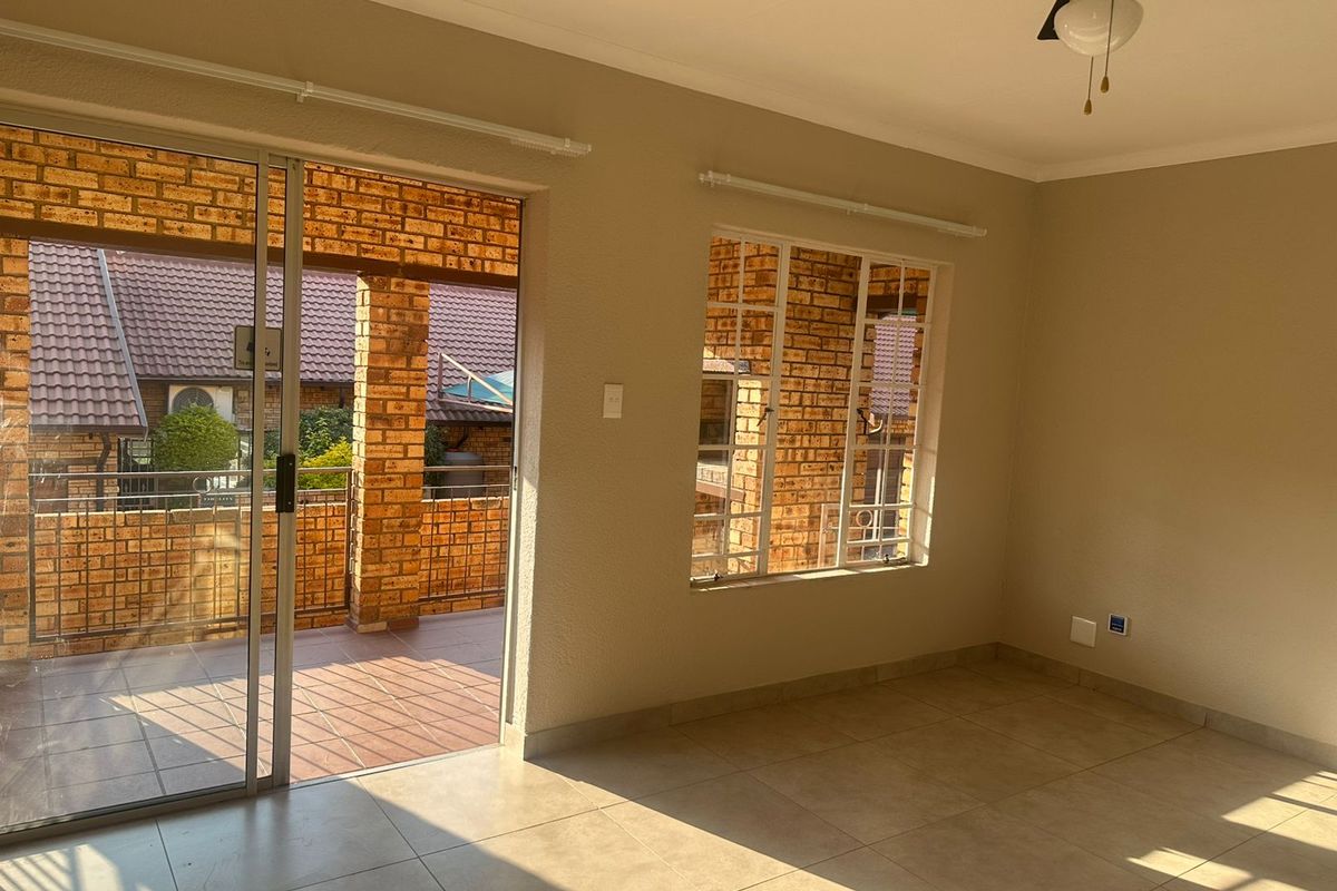 An empty, well-lit living area featuring neutral tiled flooring, a ceiling fan, and direct access to a covered patio through a sliding glass door.