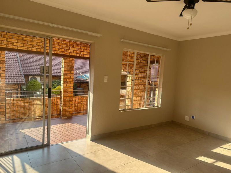 An empty, well-lit living area featuring neutral tiled flooring, a ceiling fan, and direct access to a covered patio through a sliding glass door.