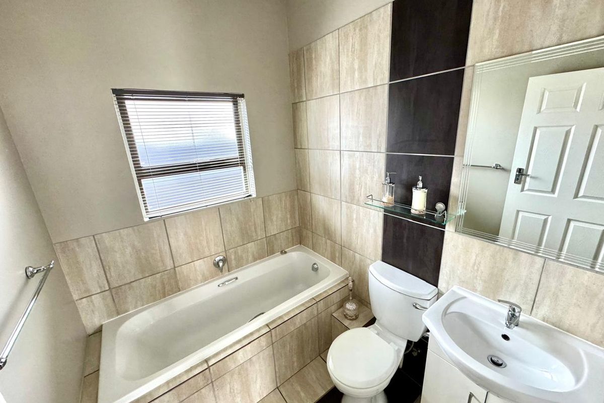 A well-maintained bathroom featuring a built-in bathtub, a modern vanity with a basin, a toilet, and neutral wall tiling with a dark accent feature.