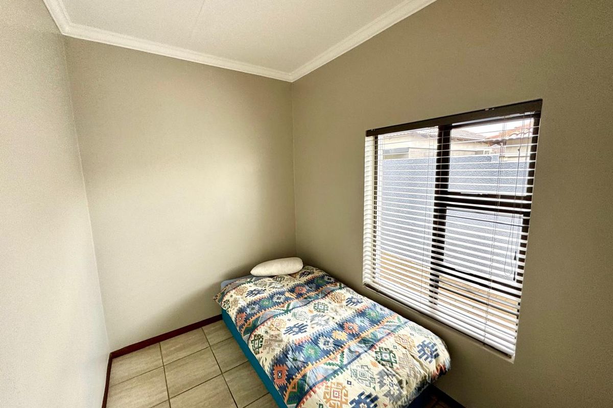 A compact bedroom featuring neutral wall tones, tiled flooring, and a window fitted with horizontal blinds.
