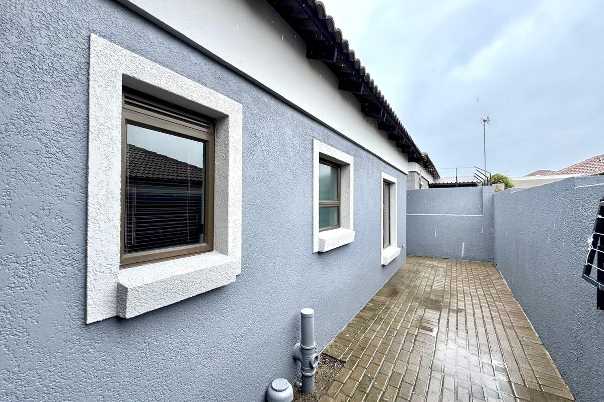 A side exterior view of the townhouse featuring a paved walkway, textured grey walls, and framed window detailing.