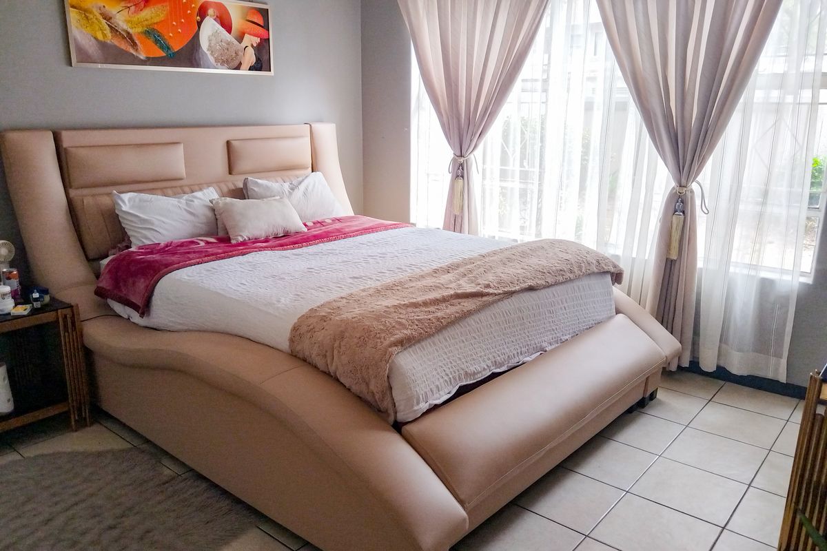 A well-lit bedroom featuring neutral tiled flooring and large windows dressed with elegant curtains, creating a comfortable and inviting sleeping space.