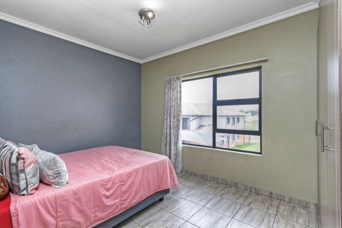 A bedroom featuring tiled flooring, built-in cupboards, and a large window providing natural light and a view of the surrounding complex.