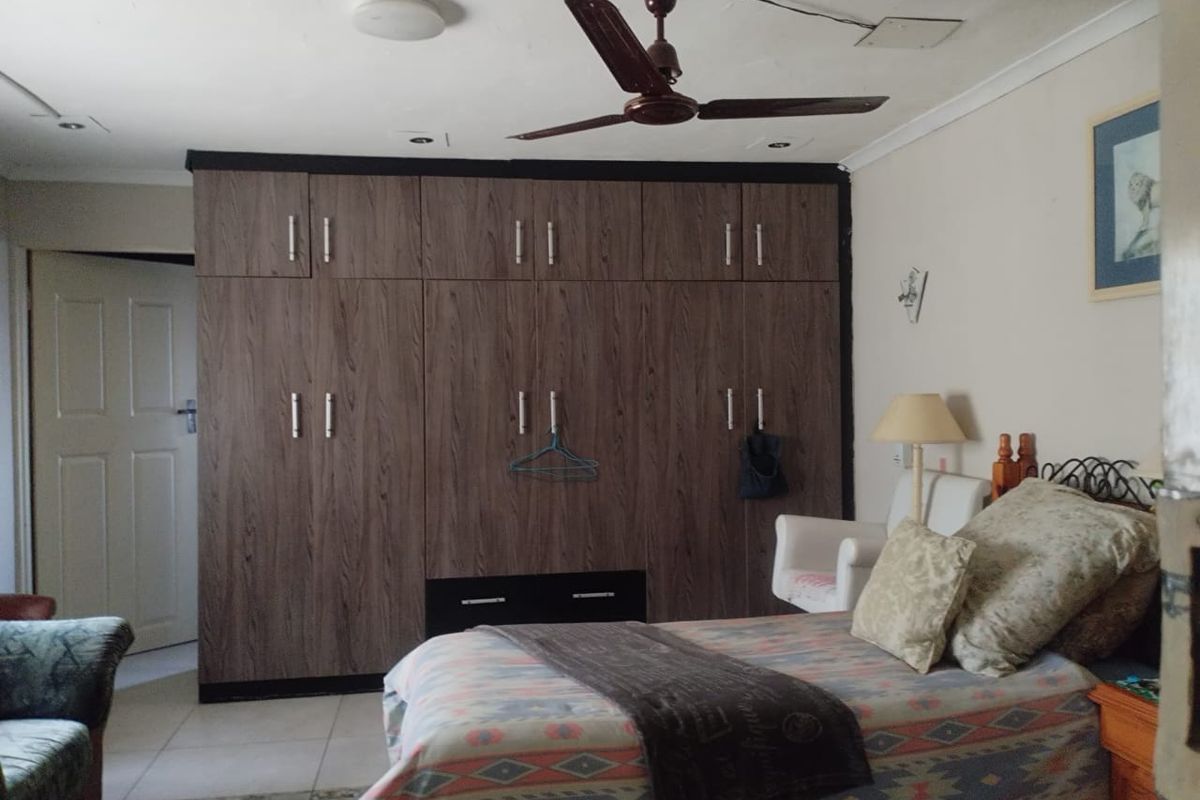 A bedroom featuring extensive dark wood-grain built-in cupboards, a ceiling fan, and tiled flooring.