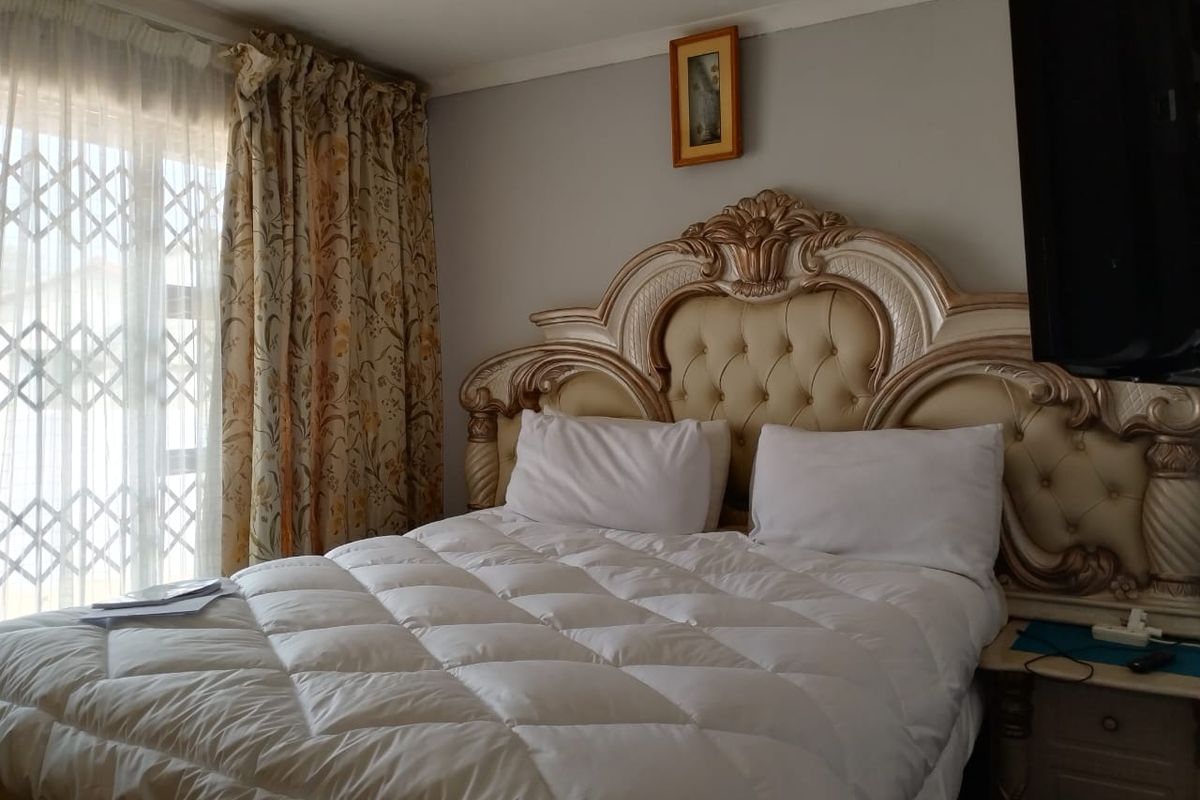 A bedroom featuring a large ornate headboard, neutral wall finishes, and a security gate over the window area.