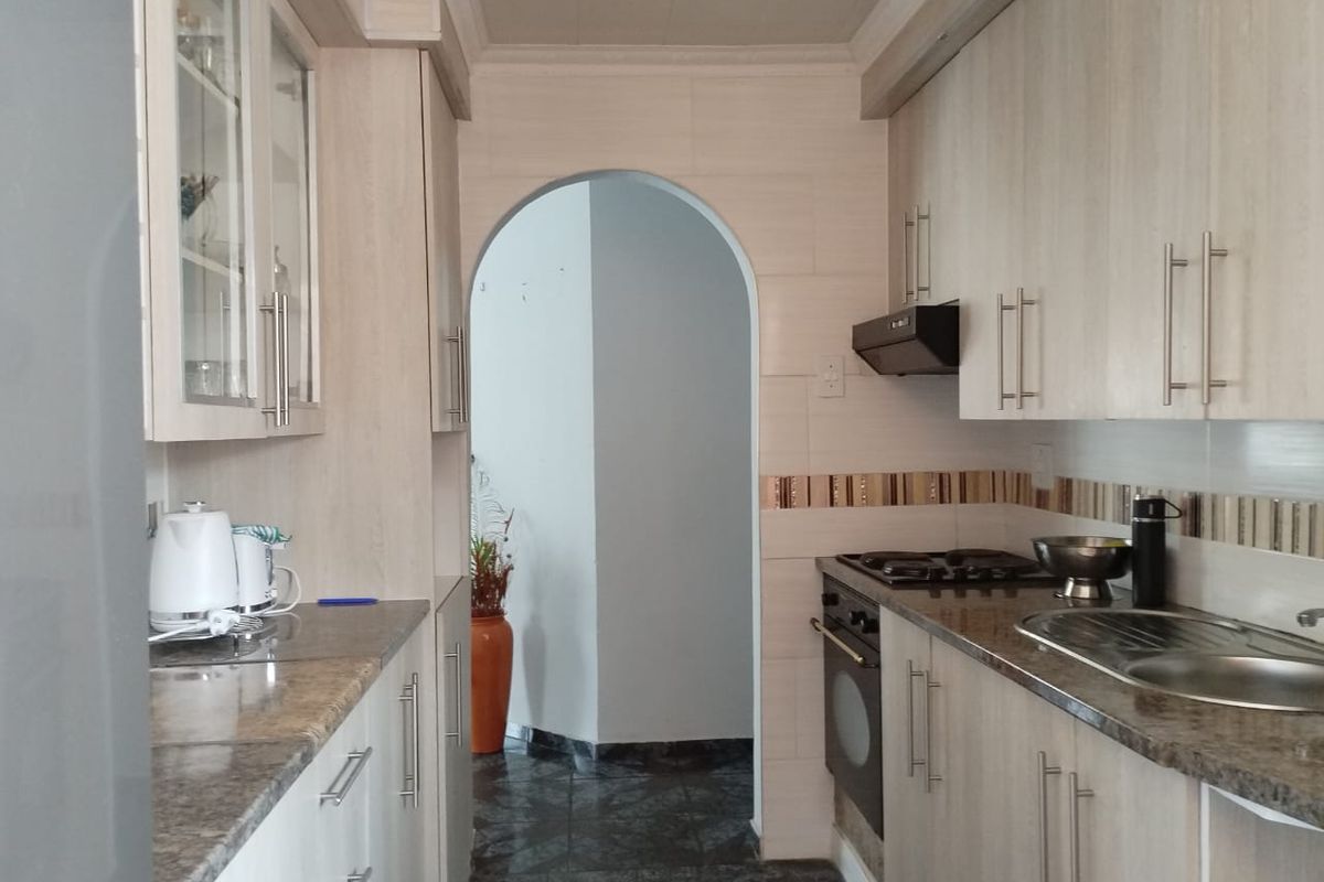 A functional galley-style kitchen featuring light wood-finish cabinetry, granite-look countertops, built-in oven, gas hob, and a distinctive arched entryway.