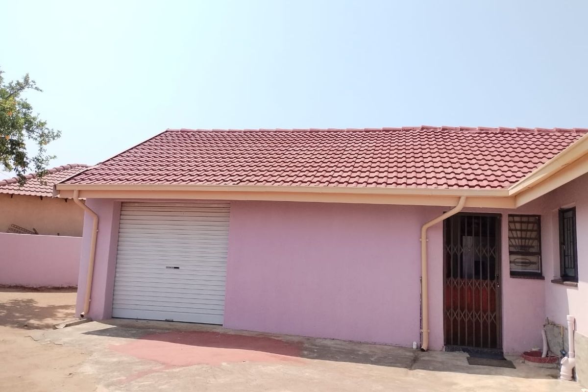 Rear exterior view of the property featuring a tiled roof, roller garage door, and secure entrance with security gate and burglar bars.