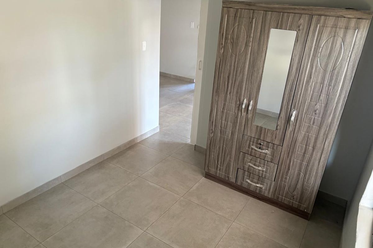 A bedroom featuring neutral floor tiles and a doorway leading to an adjacent room.