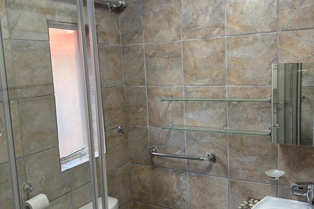 Compact bathroom featuring a glass-enclosed shower, tiled walls, a vanity with a stone-look countertop, and a wall-mounted toilet.