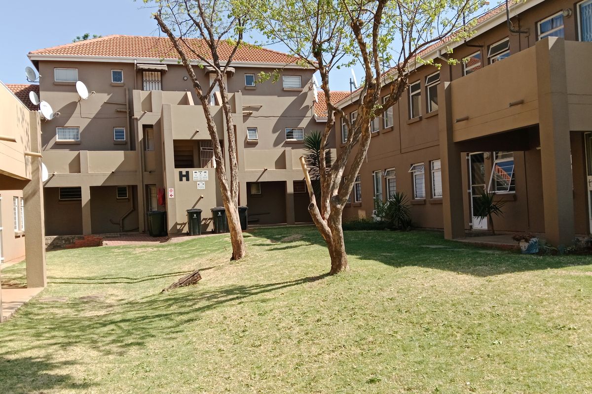 View of the apartment complex rear exterior, featuring a communal garden area, paved pathways, and multi-story residential units with tiled roofing.