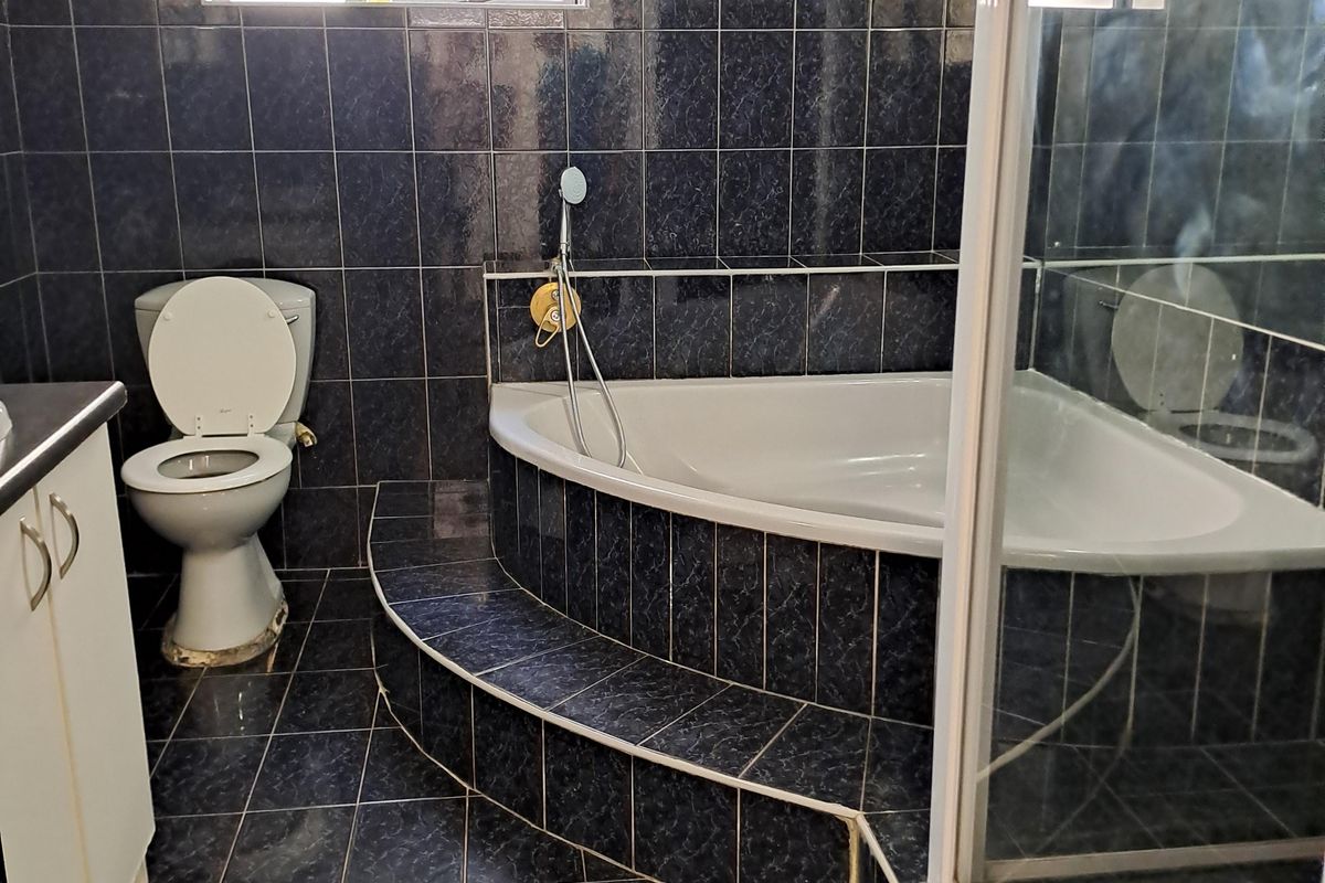A bathroom featuring a corner bathtub, separate shower enclosure, toilet, and vanity cabinet, finished with dark patterned wall and floor tiles.