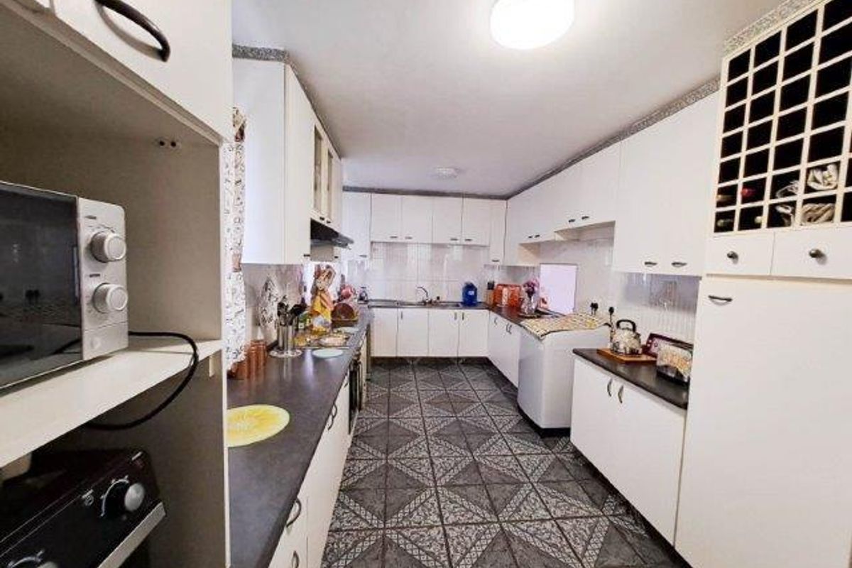 A functional kitchen featuring white cabinetry, dark laminate countertops, patterned tiled flooring, and integrated storage including a built-in wine rack.