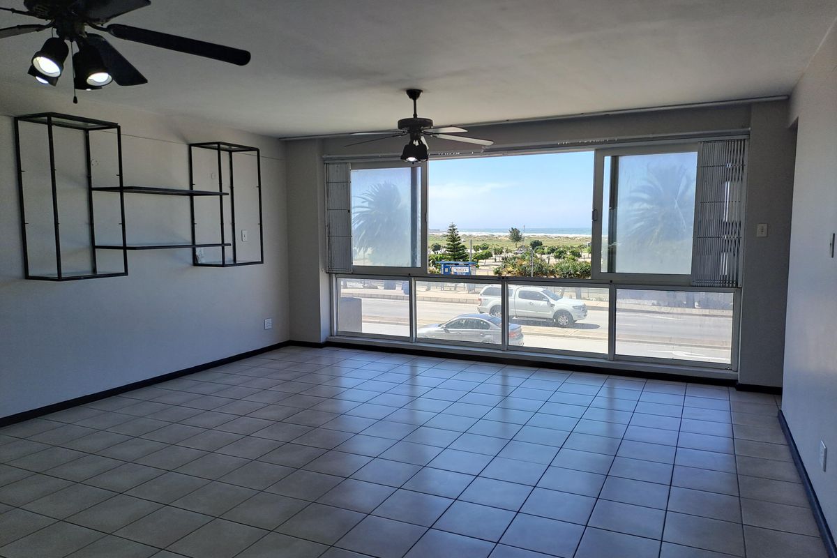 Spacious, empty living area featuring tiled floors, dual ceiling fans, and large sliding windows offering scenic coastal views.