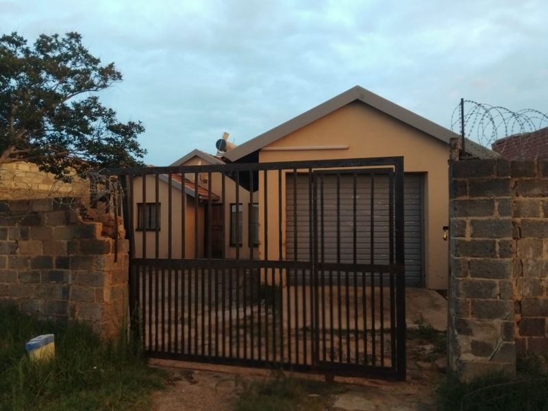 Front exterior view of a house featuring a metal driveway gate, roller garage door, and concrete block boundary wall with security razor wire.