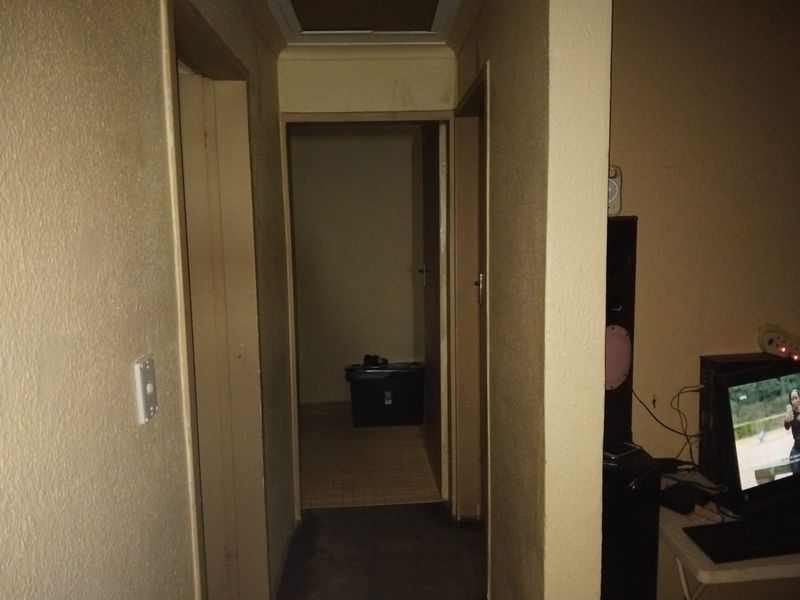 A narrow interior hallway featuring a ceiling access hatch and dated wall finishes, requiring cosmetic updates to improve the overall aesthetic.