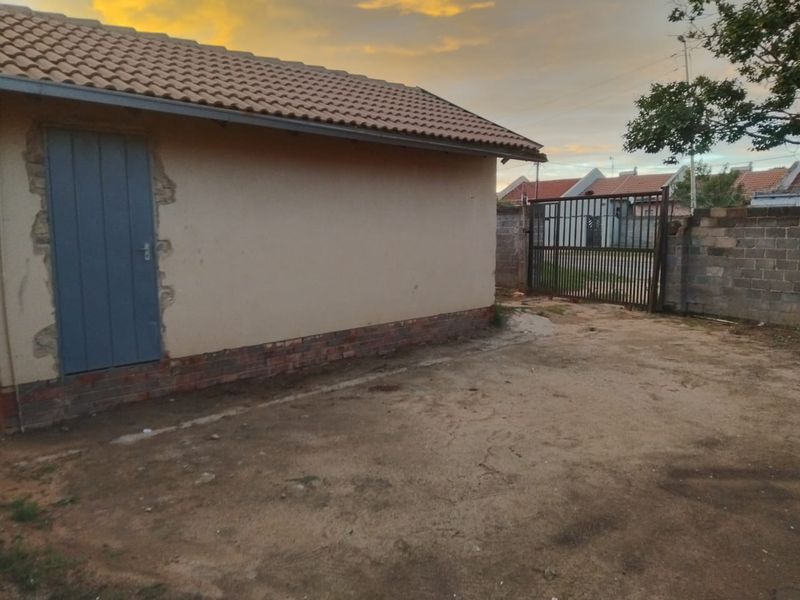 Rear exterior view of the property featuring a tiled roof, plain wall finish, and a metal security gate leading to the street.