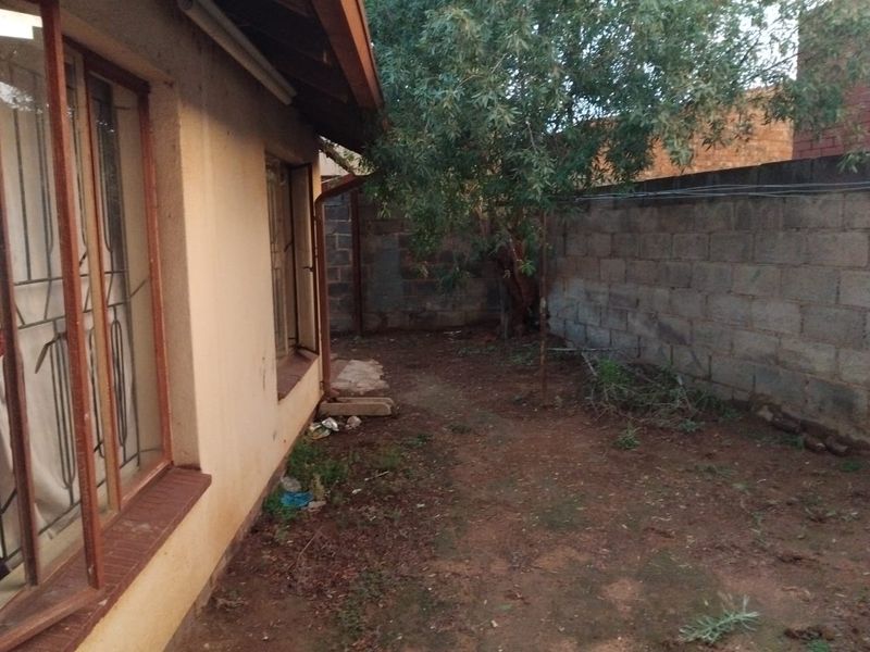 A rear exterior view of the property featuring a concrete block boundary wall and basic ground area requiring landscaping.