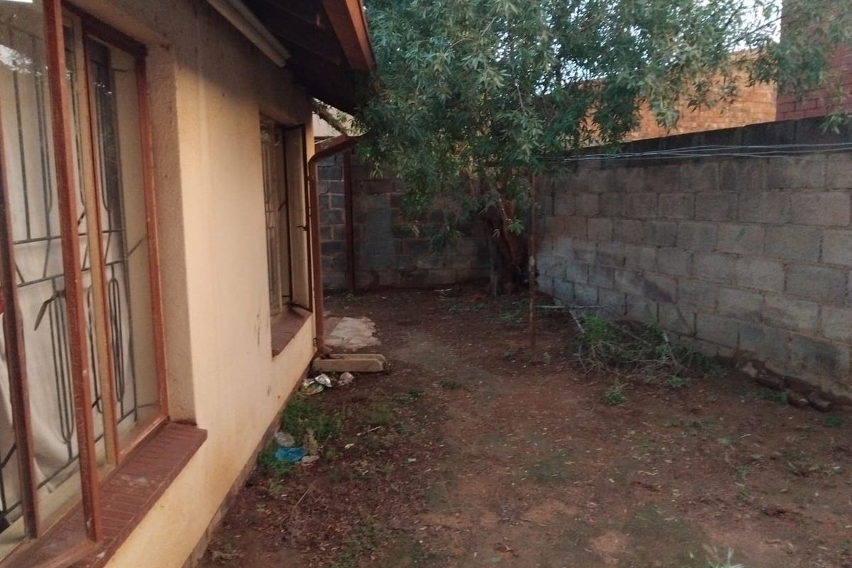A rear exterior view of the property featuring a concrete block boundary wall and basic ground area requiring landscaping.