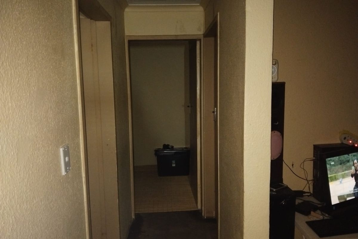 A narrow interior hallway featuring a ceiling access hatch and dated wall finishes, requiring cosmetic updates to improve the overall aesthetic.