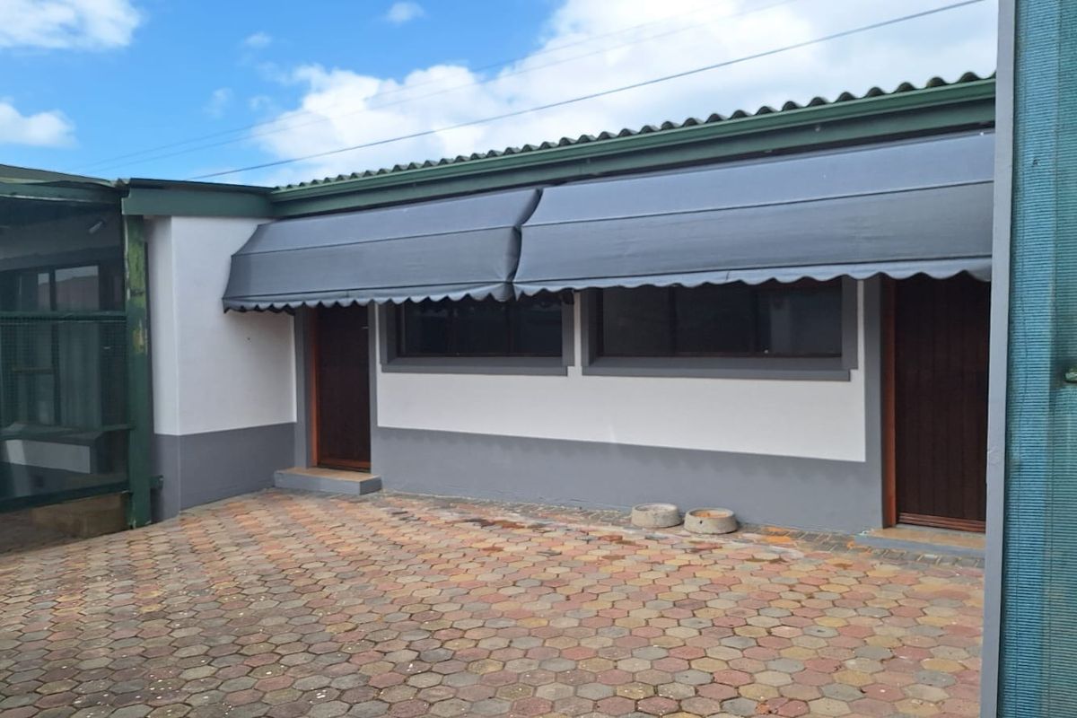 A paved rear courtyard area featuring a covered patio section with retractable awnings, providing access to the main dwelling.