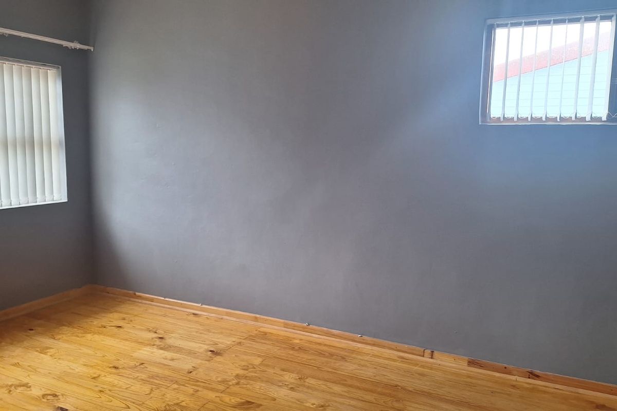 An empty bedroom featuring polished wooden flooring, grey painted walls, and vertical window blinds.