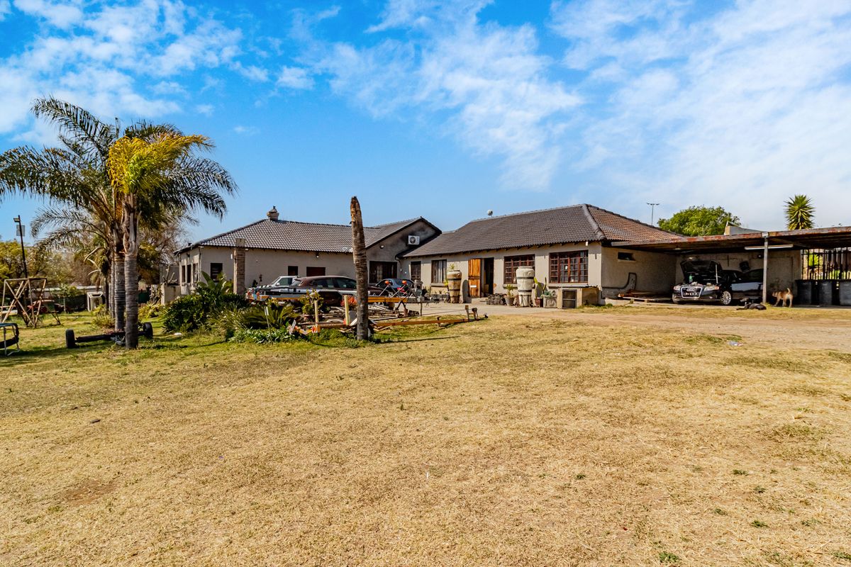 Rear view of the small holding property featuring a tiled roof dwelling, attached carport, and expansive grounds.