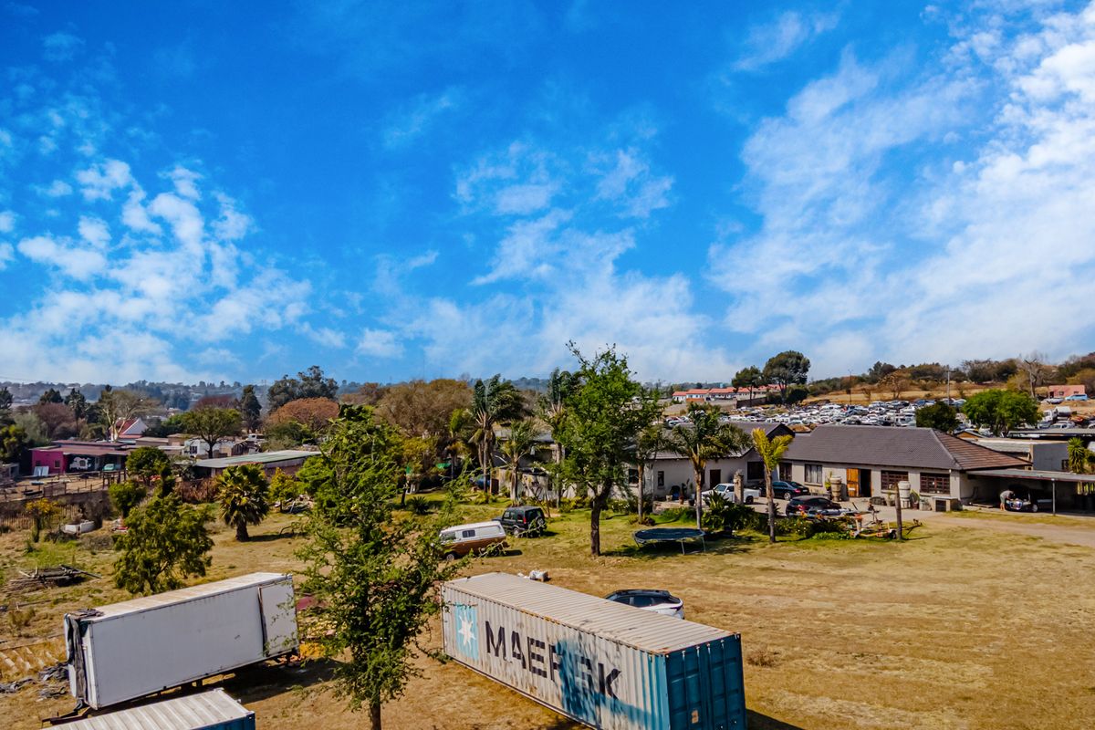Aerial view of a small holding property featuring a main dwelling with a pitched roof, covered parking areas, and expansive grounds.