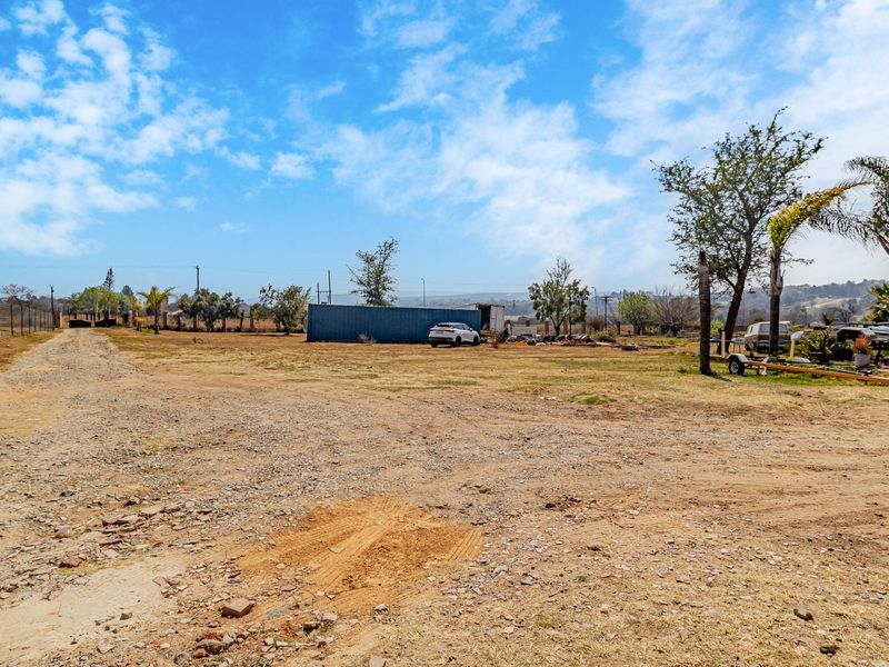 Expansive open land area featuring a gravel driveway, perimeter wire fencing, and a large storage container on a small holding property.