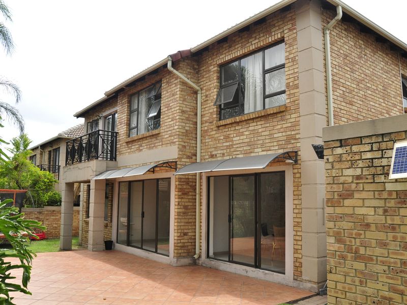 Rear view of a double-story townhouse featuring face brick construction, a tiled patio, sliding glass doors, and an upper-level balcony.