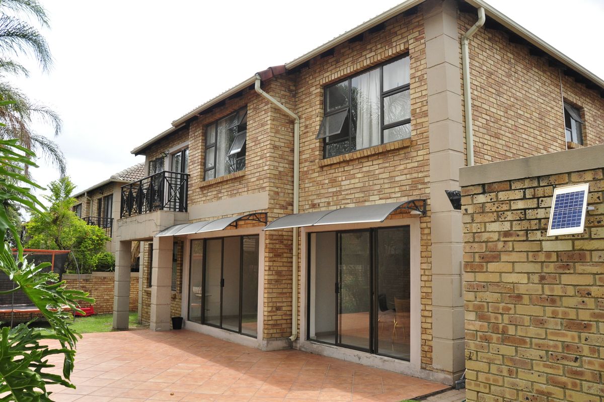 Rear view of a double-story townhouse featuring face brick construction, a tiled patio, sliding glass doors, and an upper-level balcony.