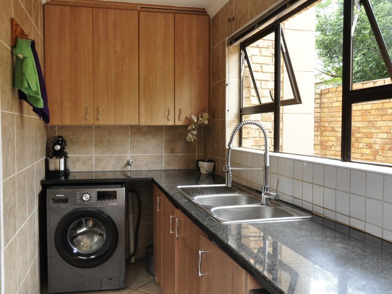 A functional laundry room featuring wood-finish cabinetry, granite countertops, a double sink with a modern mixer tap, and tiled wall finishes.