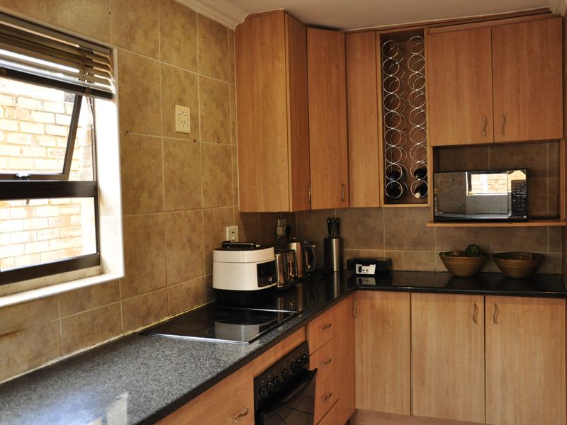 A functional kitchen featuring wood-look laminate cabinetry, dark granite countertops, a built-in oven, electric hob, and a dedicated wine storage rack.