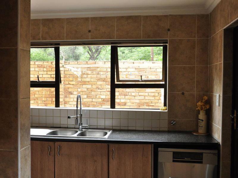 A functional kitchen area featuring a double bowl sink, granite countertops, and tiled splashbacks with a view of the rear garden.