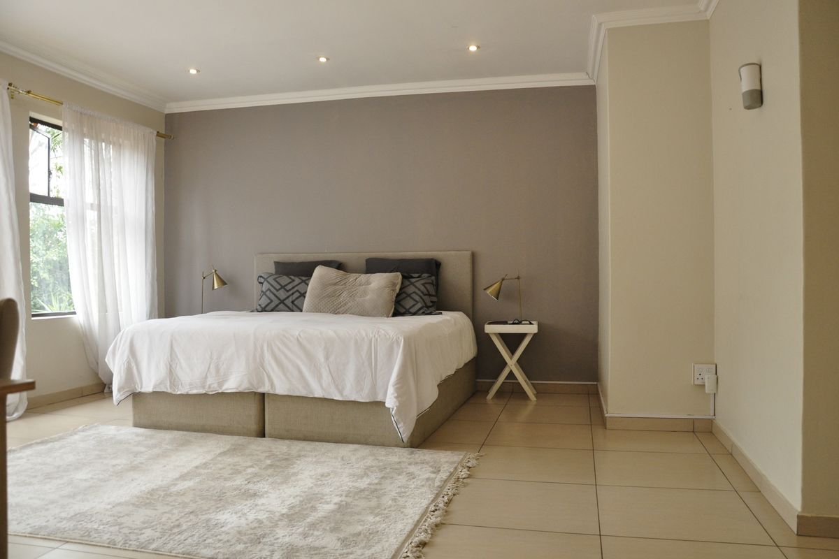 A well-maintained bedroom featuring neutral tiled flooring, recessed downlighting, and a feature wall, offering a clean and comfortable living space.