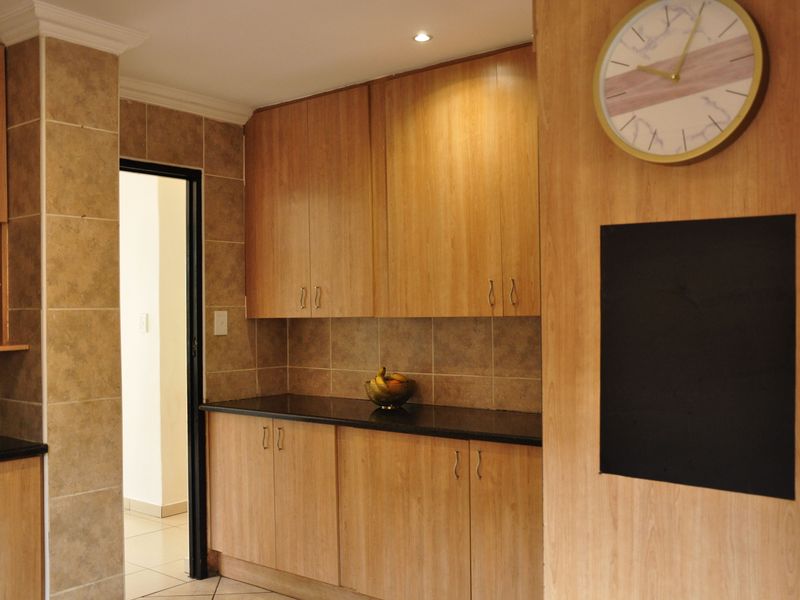 A functional kitchen area featuring light wood-finish cabinetry, dark granite countertops, and neutral tiled backsplash with integrated downlighting.