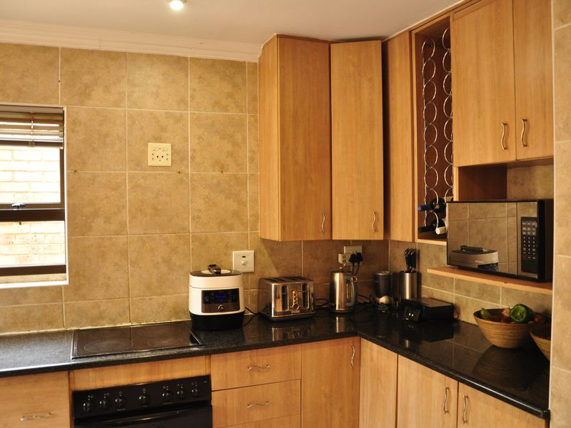 A functional kitchen featuring wooden cabinetry, granite countertops, a built-in oven, electric hob, and tiled backsplash with integrated storage solutions.
