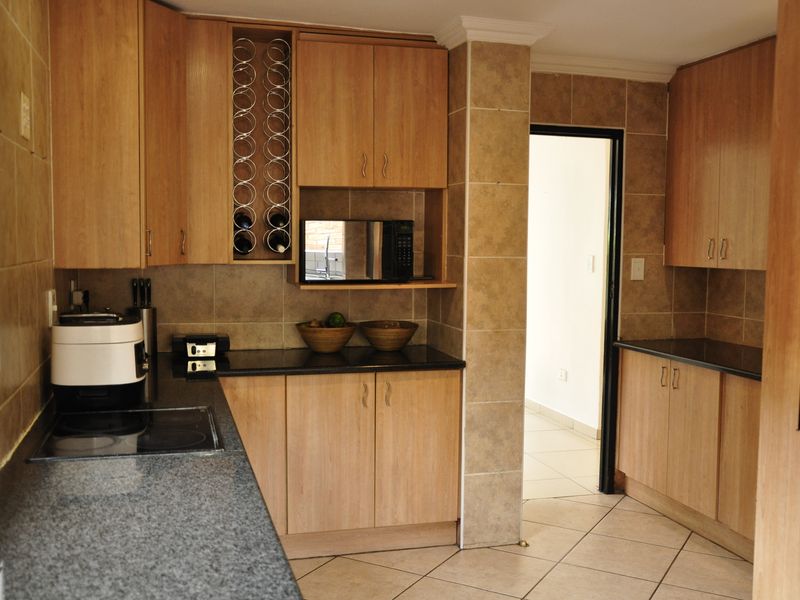 A functional kitchen featuring light wood laminate cabinetry, dark granite countertops, a built-in microwave, and tiled finishes throughout.