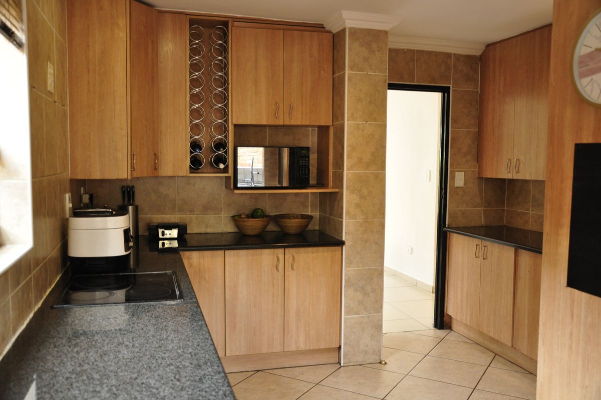 A functional kitchen featuring light wood laminate cabinetry, dark granite countertops, a built-in microwave, and tiled finishes throughout.