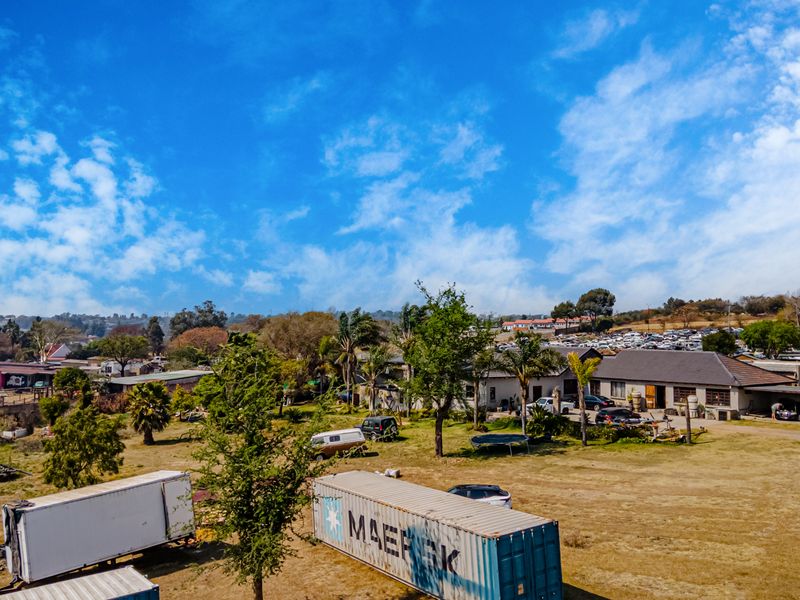 Aerial view of a small holding property featuring a main dwelling with a pitched roof, covered parking areas, and expansive grounds.